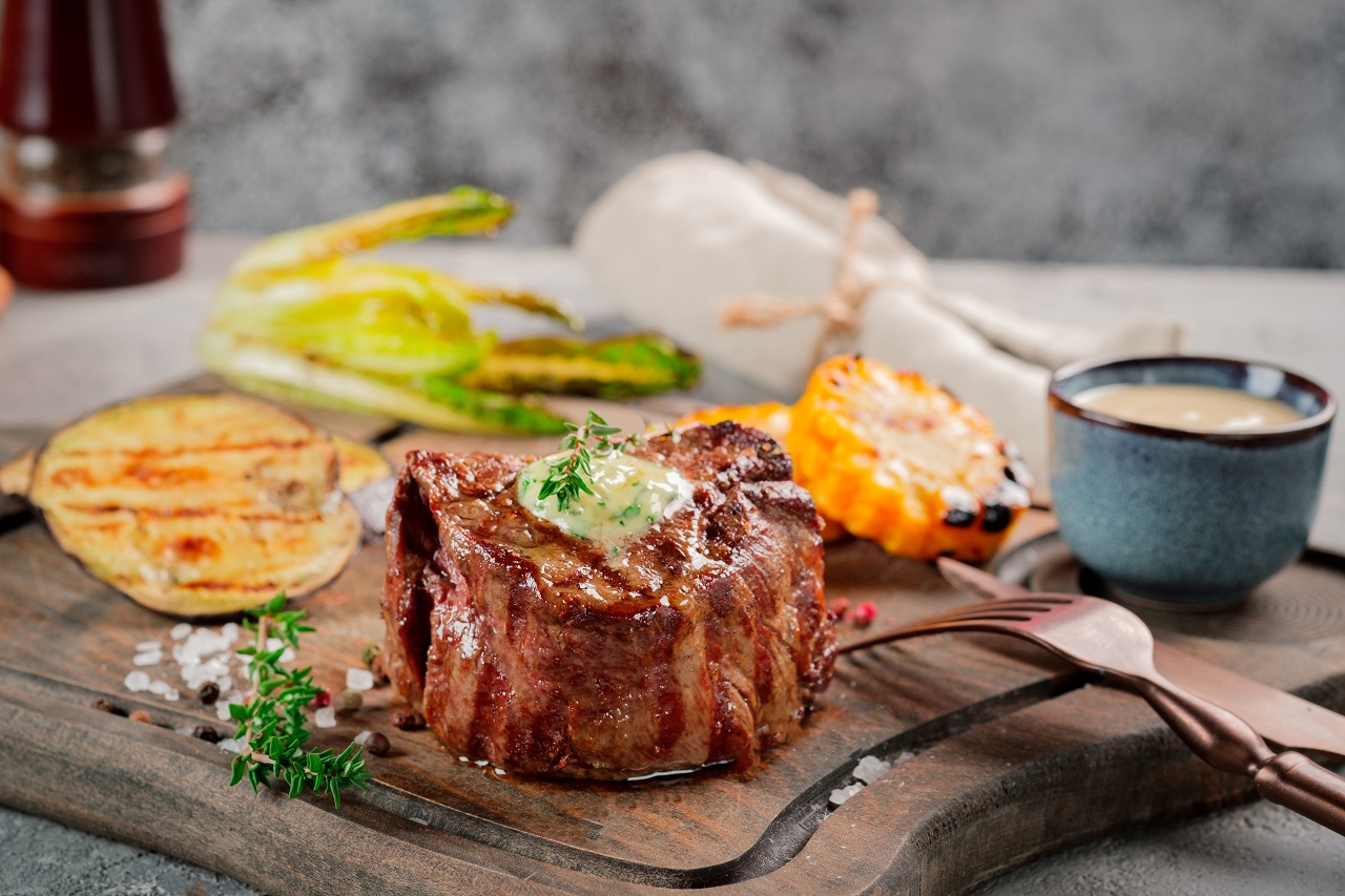 Large-grilled-Filet-Mignon-steak-with-butter-and-thyme-served-on-a-wooden-board.-Grilled-meat-dish-with-vegetables
