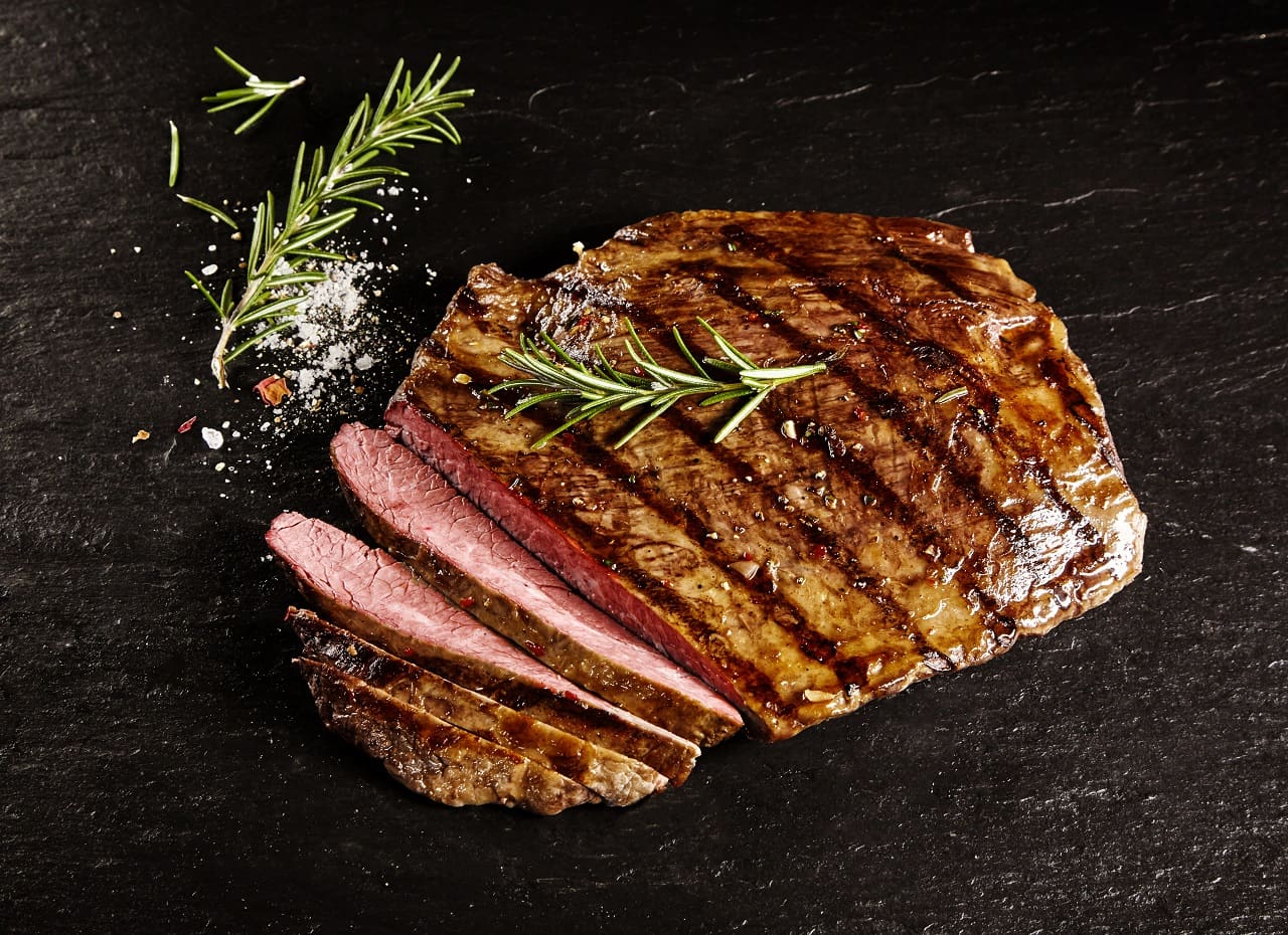 Single-roasted-medium-rare-sliced-flank-beef-piece-with-rosemary-over-dark-table-background