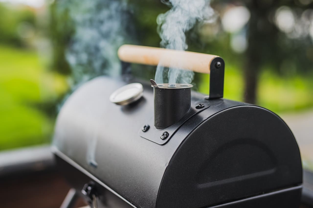 Smoke-coming-out-of-a-smokestack-of-a-small-black-smoker-grill-or-barbecue-on-green-background